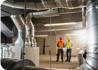 Albos HVAC crew working beneath large commercial spiral ductwork on an industrial job site